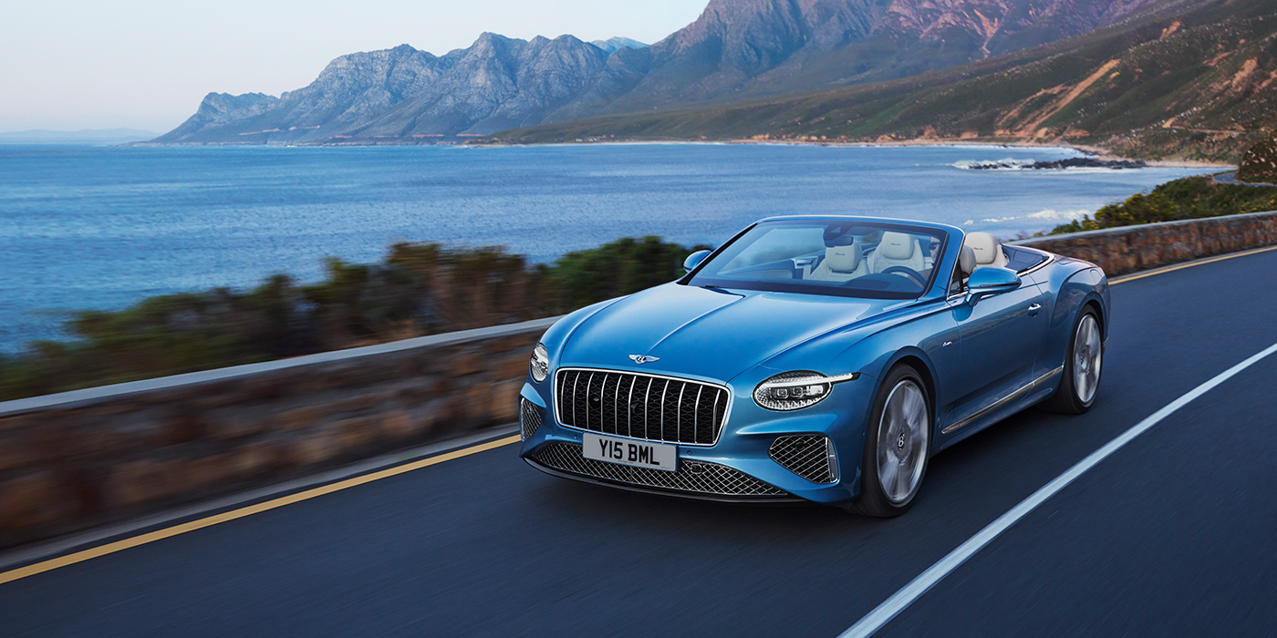 Bentley Köln New Bentley Continental GTC Azure convertible in Light Windsor blue paint with 22 inch Azure wheels and chrome grill, driving dynamically by the sea