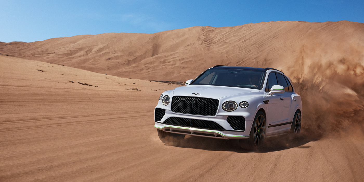 Bentley Köln Bentley Bentayga Speed SUV front three quarter in Snow Quarts Pearlescent by Mulliner white paint driving dynamically through the desert