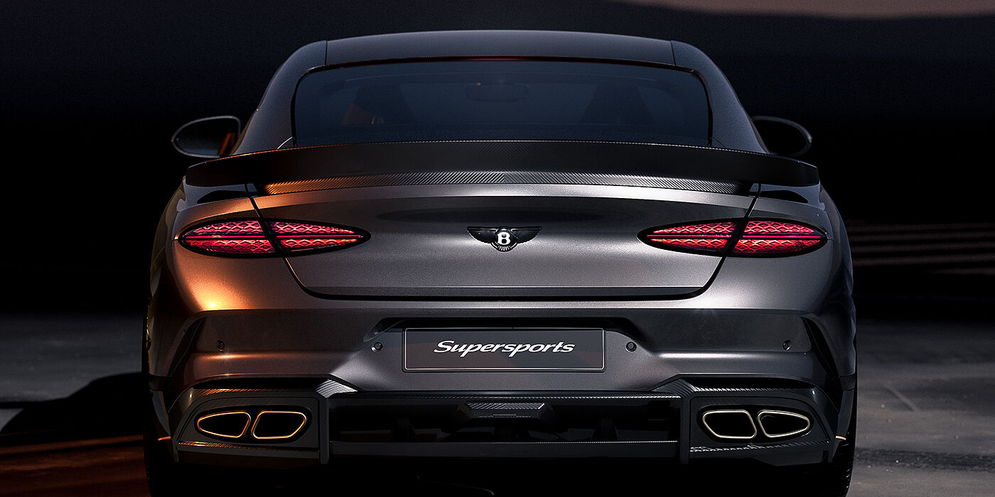 Bentley Köln Bentley Supersports rear view with illuminated rear lamps, spoiler and black Bentley badge in Anthracite paint against a dark grey and red background