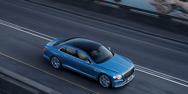 Bentley Köln New Bentley Flying Spur Azure sedan in Light windsor blue paint by Mulliner, with 22 inch Azure wheels seen from overhead driving dynamically on a country road
