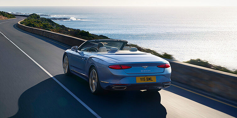 Bentley Köln New Bentley Continental GTC Azure convertible rear view in Light Windsor blue paint with 22 inch ten spoke wheels driving dynamically on an ocean road in the sunshine