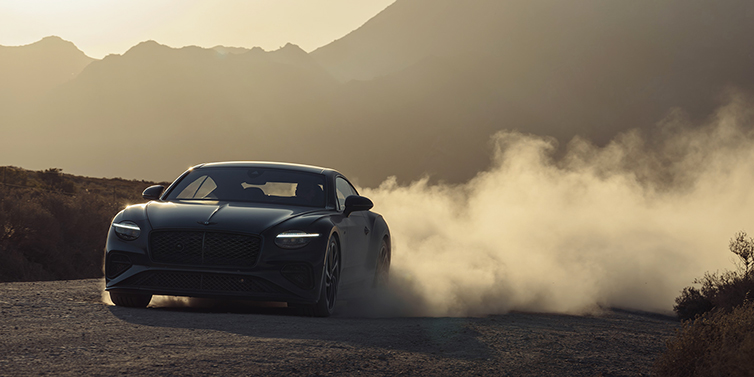 Bentley Köln Bentley Continental GT coupe in Thunder paint front 3/4 driving with dust trail at sunset