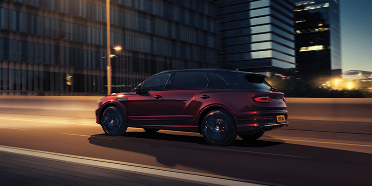 Bentley Köln Bentley Bentayga Extended Wheelbase Mulliner SUV in Cricket Ball red paint driving dynamically in city at night